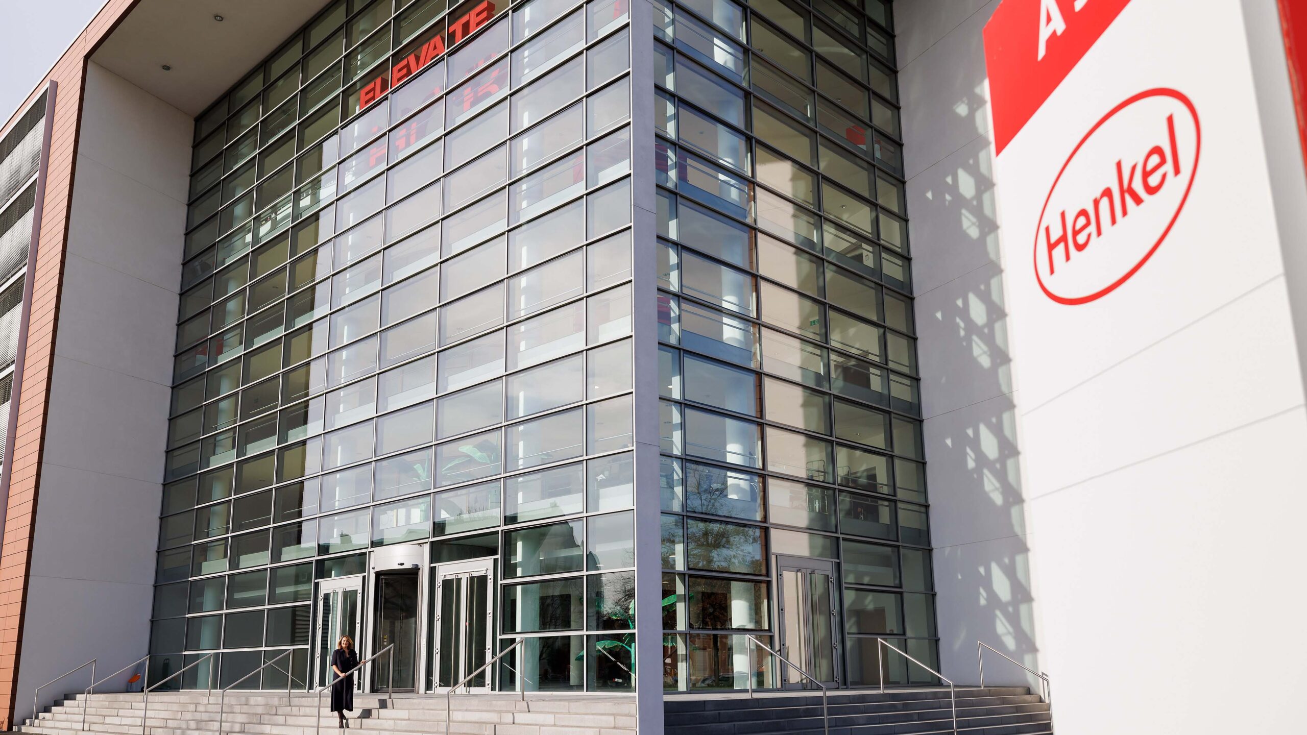 Sylvie Nicol auf den Treppen des modernen quadratischen Atrium-Gebäudes A 33 in Düsseldorf-Holthausen. Am Traditionsstandort spiegelt Industriearchitektur verschiedener Epochen die lange Erfolgsgeschichte von Henkel wider.